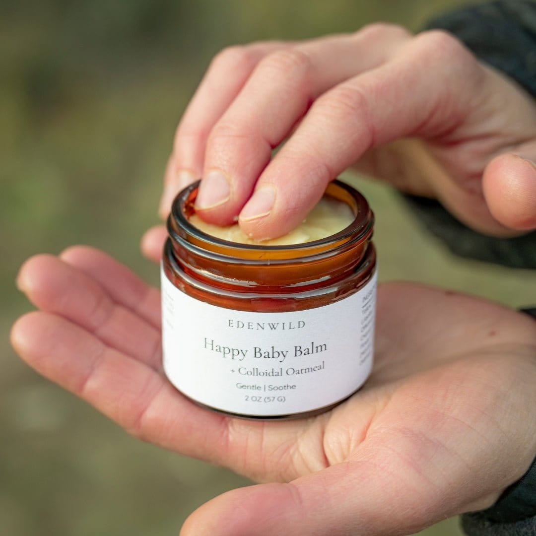 Hands holding open jar of Edenwild Happy Baby Balm outdoors — fragrance-free balm for eczema relief and sensitive skin nourishment for the whole family
