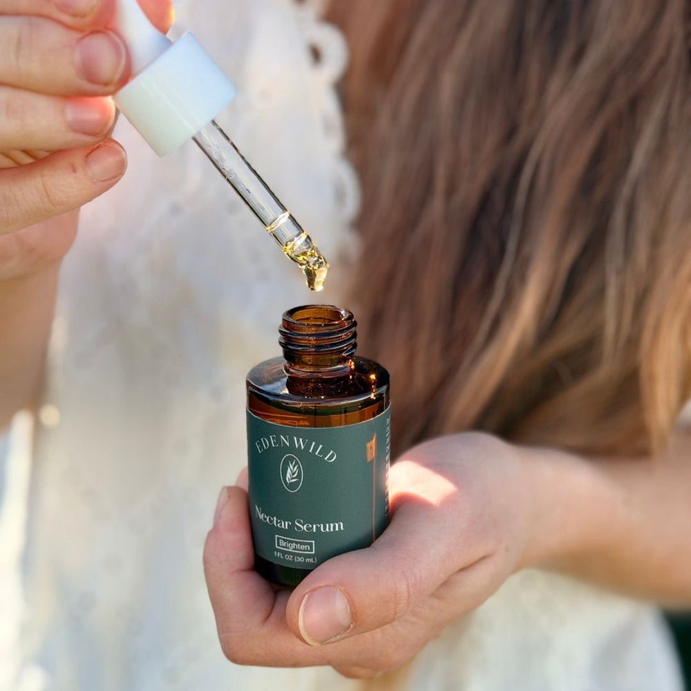 Woman holding an amber bottle of Edenwild facial serum with a glass dropper of golden oil above the opening, highlighting ancestral skincare.