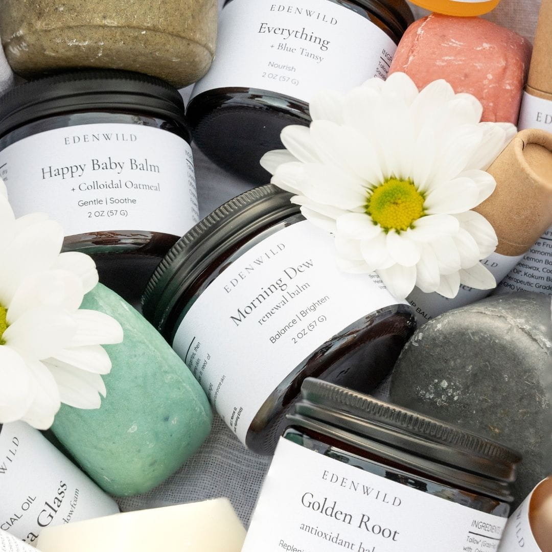 Edenwild natural skincare collection — Happy Baby Balm, Morning Dew tallow balm, Everything Balm, and Golden Root antioxidant balm with white daisy florals