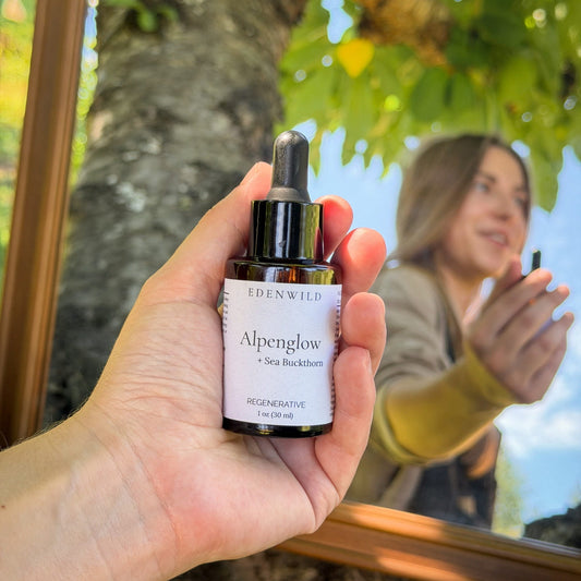 Edenwild Alpenglow regenerative face serum with sea buckthorn — held up against a window reflecting a woman outdoors in natural light