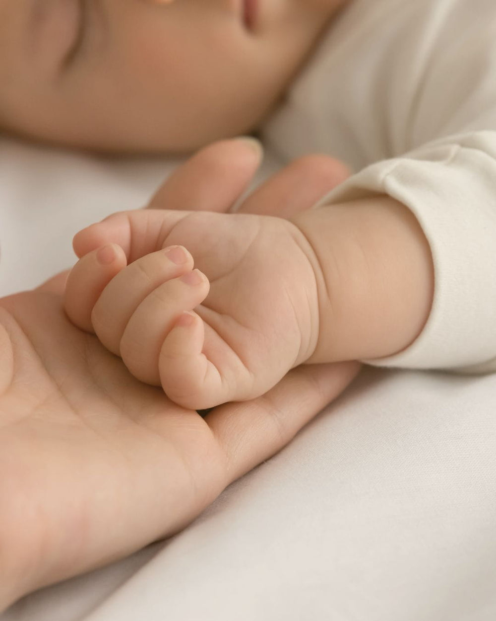 Sleeping baby resting hand in mother's palm featured in Edenwild baby eczema relief article on natural ingredients for sensitive and eczema-prone baby skin
