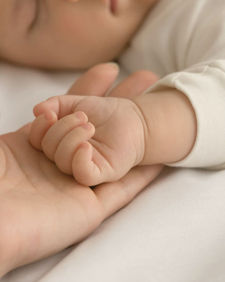 Sleeping baby resting hand in mother's palm featured in Edenwild baby eczema relief article on natural ingredients for sensitive and eczema-prone baby skin