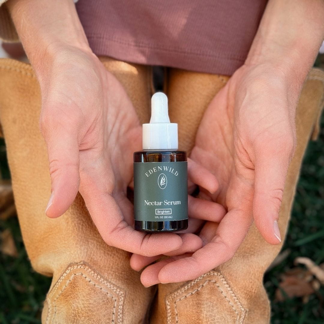 Edenwild Nectar bakuchiol face serum in an amber glass dropper bottle, cradled in hands over tan boots outdoors.