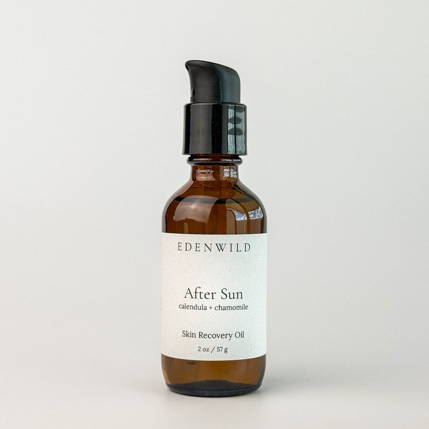Edenwild After Sun Skin Recovery Oil with calendula and chamomile in amber pump bottle on grey background — botanical after sun oil for skin repair and redness relief