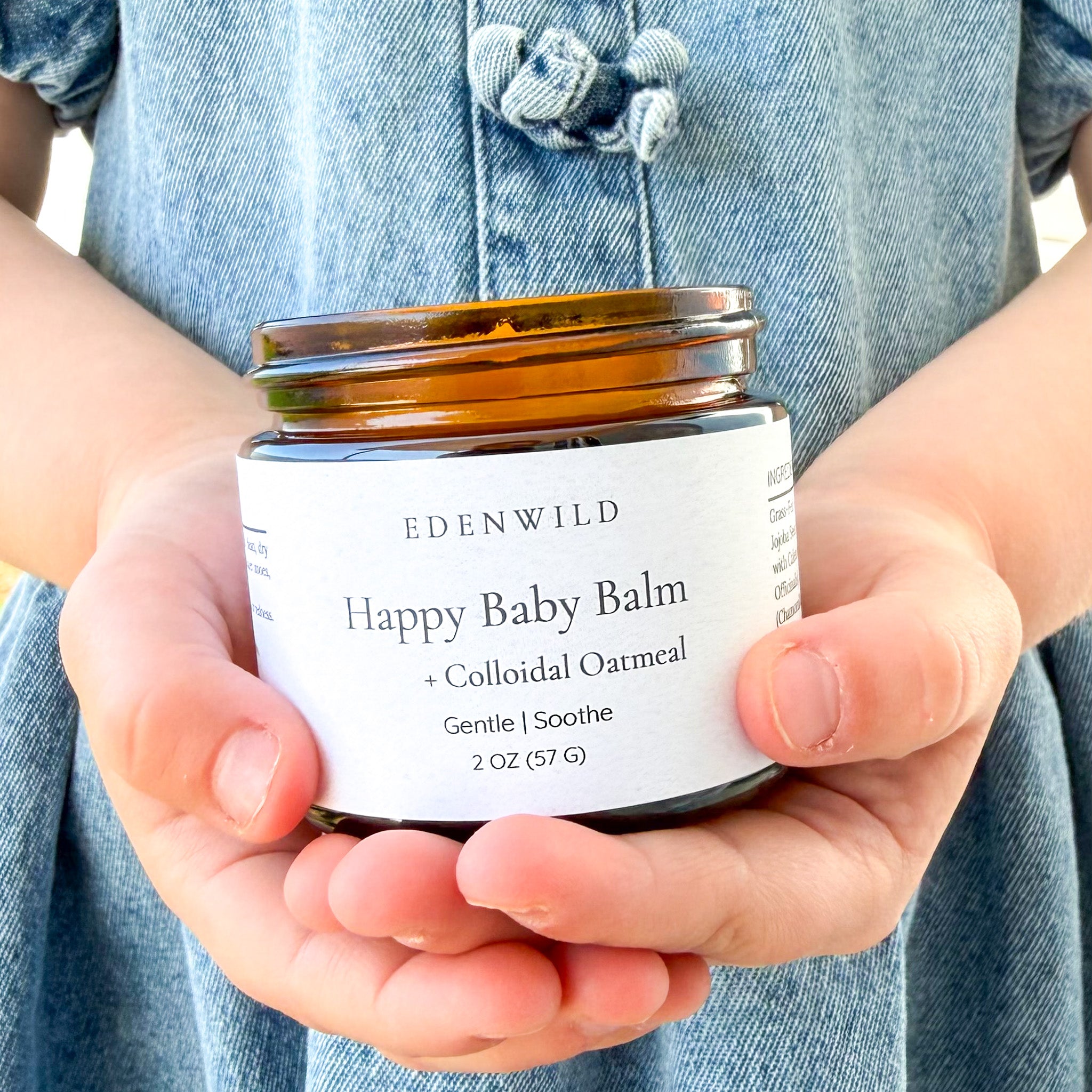 Hands holding a jar of Edenwild Happy Baby Balm with Colloidal Oatmeal to help soothe and protect sensitive and eczema-prone skin