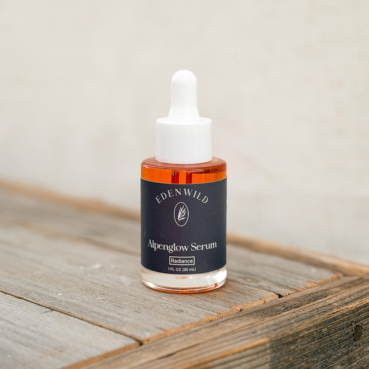 Edenwild Alpenglow Serum, an ancestral skincare serum in a glass bottle with a white dropper and black label, displayed on rustic wood.