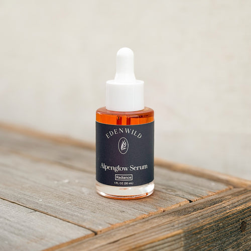 Edenwild Alpenglow Serum, an ancestral skincare serum in a glass bottle with a white dropper and black label, displayed on rustic wood.