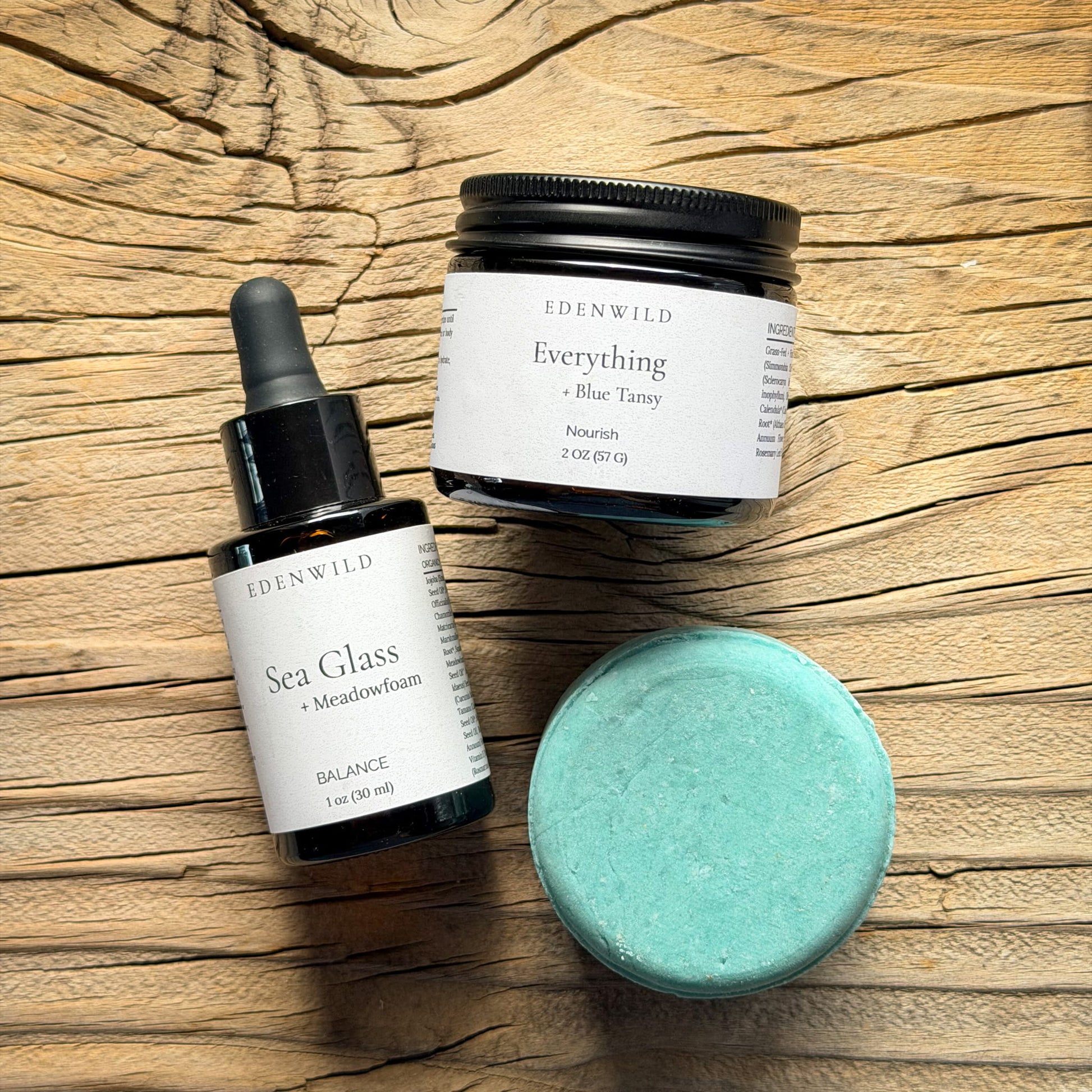 Edenwild Sea Glass botanical face serum and Everything Blue Tansy tallow balm with Balance shampoo bar on rustic wood surface