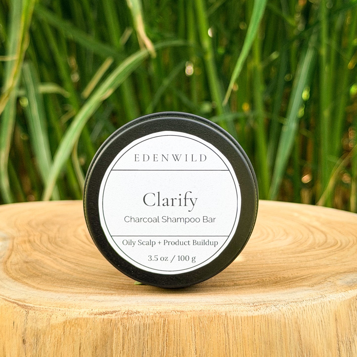 Edenwild Clarify Charcoal Shampoo Bar for oily scalp and product buildup displayed on a wood stump with green grass background
