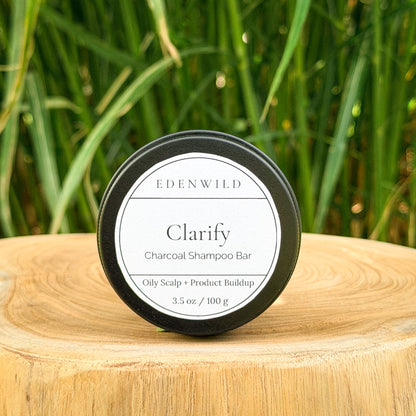 Edenwild Clarify Charcoal Shampoo Bar for oily scalp and product buildup displayed on a wood stump with green grass background
