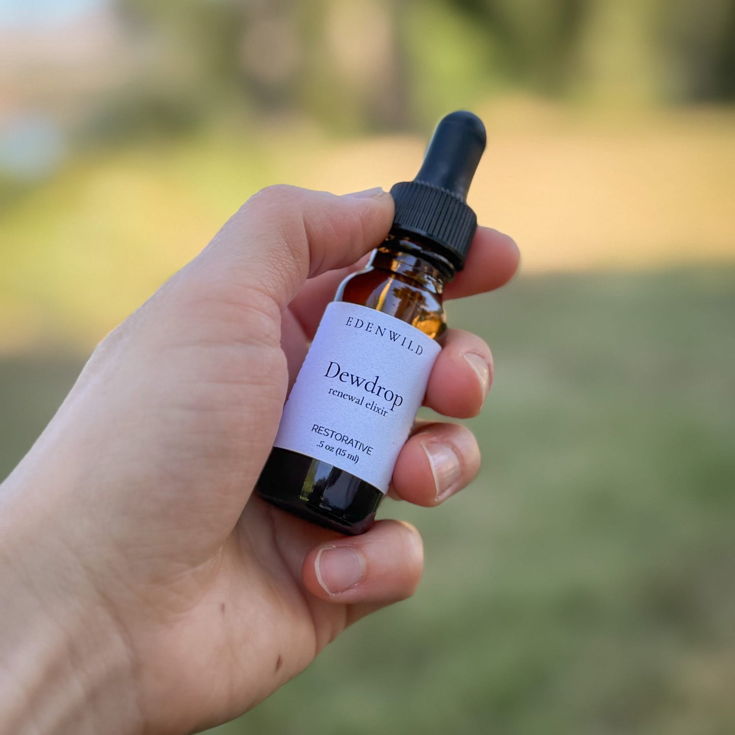 Hand holding Edenwild Dewdrop Renewal Elixir face serum 0.5 oz outdoors — restorative botanical serum for dry, sensitive, and aging skin