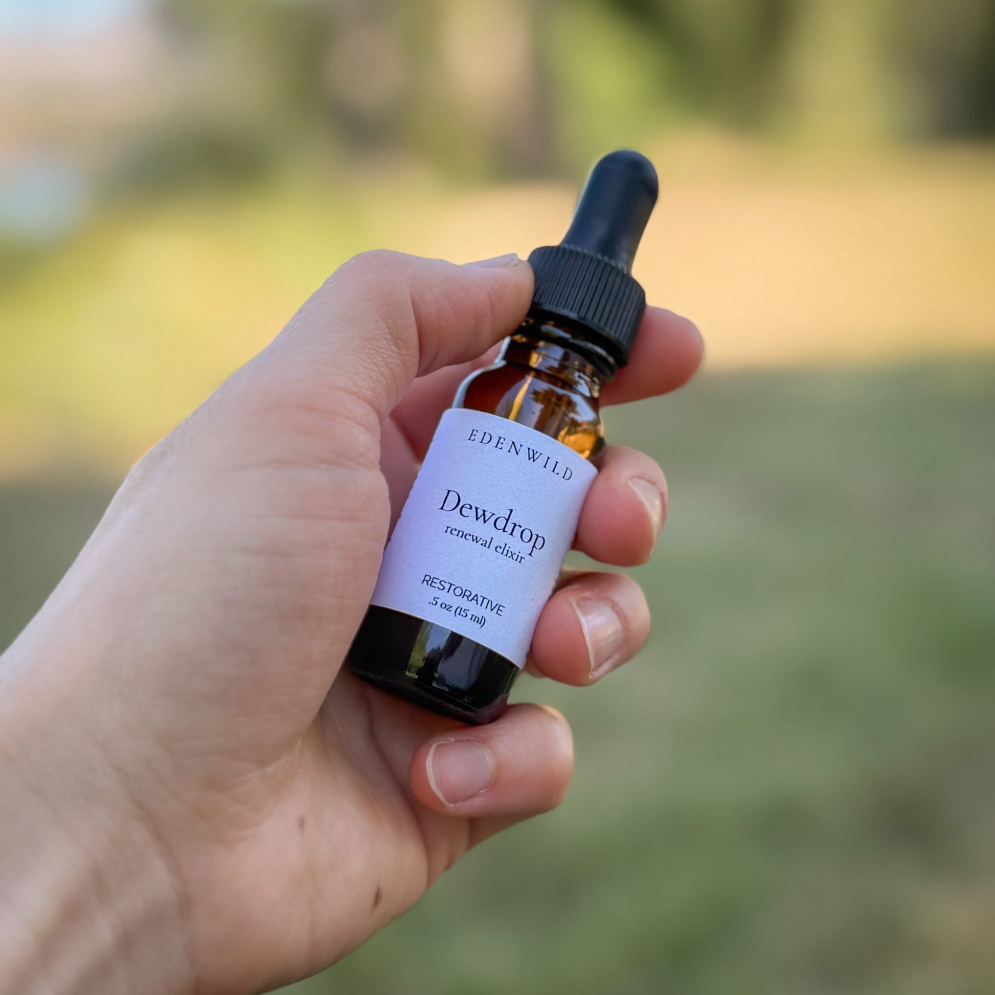 Hand holding Edenwild Dewdrop Renewal Elixir face serum 0.5 oz outdoors — restorative botanical serum for dry, sensitive, and aging skin