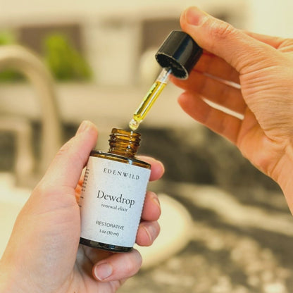 Hands holding Edenwild Dewdrop Renewal Elixir dropper bottle, a restorative face serum used to help restore and renew skin naturally