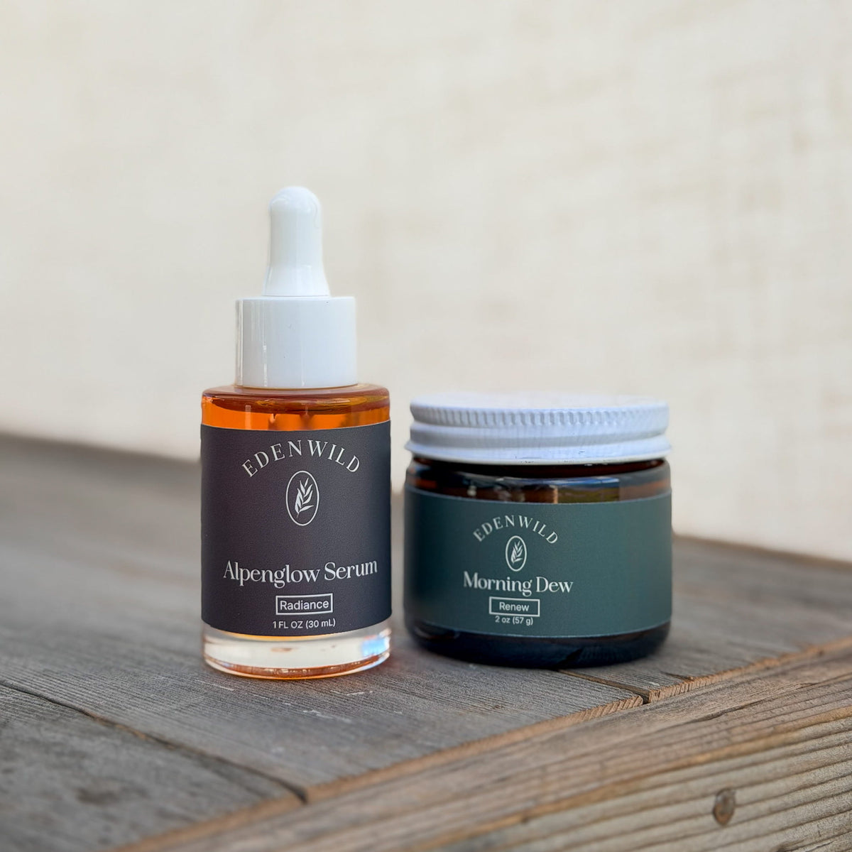 Edenwild Alpenglow Serum dropper bottle and Morning Dew balm jar on a rustic wooden surface, paired as an ancestral skincare routine.