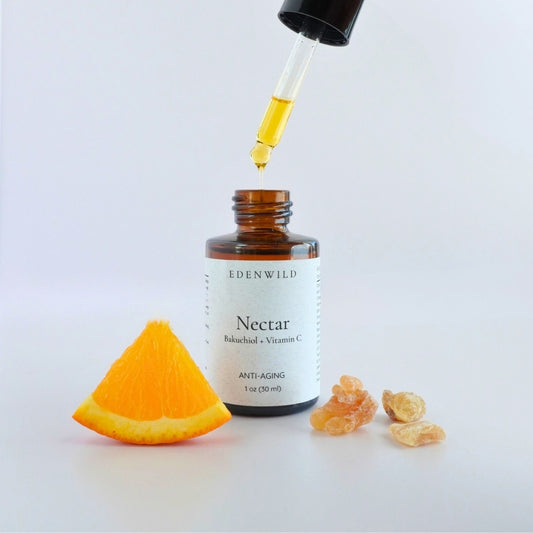 Elegant flat lay of Nectar Face Serum bottle with fresh orange slice and golden frankincense resin on white background, showcasing key ingredients in Edenwild Nectar Face Serum to help brighten and rejuvenate mature skin