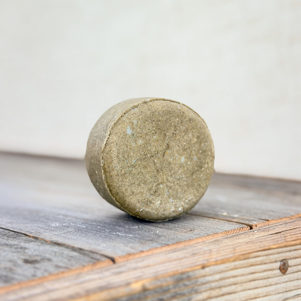 Edenwild Restore nettle and tea tree shampoo bar standing upright on weathered wood, showing its round shape and textured sage-green surface.