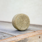 Edenwild Restore nettle and tea tree shampoo bar standing upright on weathered wood, showing its round shape and textured sage-green surface.