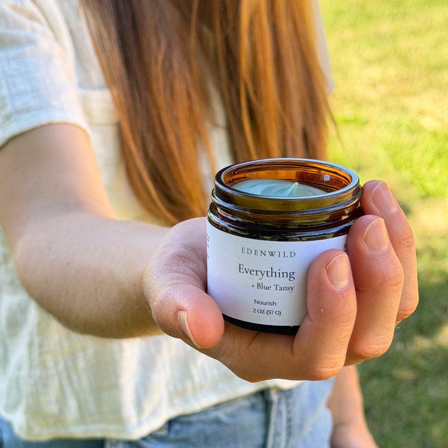 Woman's hand holding open jar of Edenwild Everything grass-fed and grass-finished tallow balm with blue tansy, ancestral skincare for sensitive skin