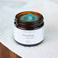 Open jar of grass-fed tallow balm with creamy texture displayed on white towel and dark wood surface, used in Edenwild Everything + Blue Tansy Balm to help calm eczema and sensitive skin