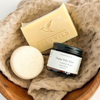 Edenwild Gentle Skin Trio — Happy Baby Balm jar, Happy Baby Soap Bar, and Bare shampoo bar arranged in wooden bowl with textured linen cloth