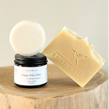 Happy Baby Balm jar with shampoo bar stacked on top and Happy Baby Soap Bar leaning against wood stump — Edenwild natural sensitive skincare bundle