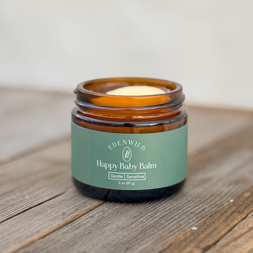 Open jar of Edenwild Happy Baby Tallow Balm, an ancestral skincare balm for delicate skin, with a sage green label on a rustic wooden surface.