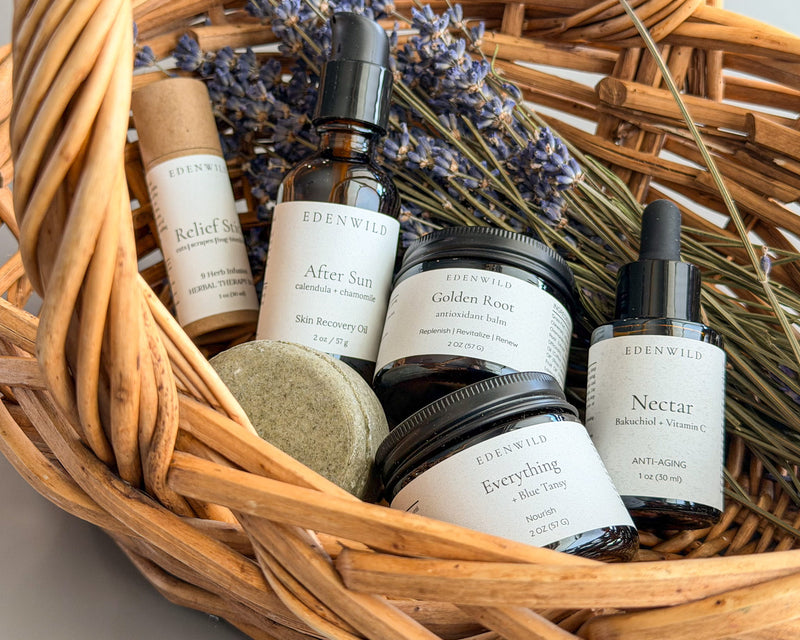 Edenwild natural skincare collection including Golden Root balm, Nectar serum, Everything balm, Relief Stick, Restore shampoo bar, and After Sun oil arranged in a wicker basket with dried lavender