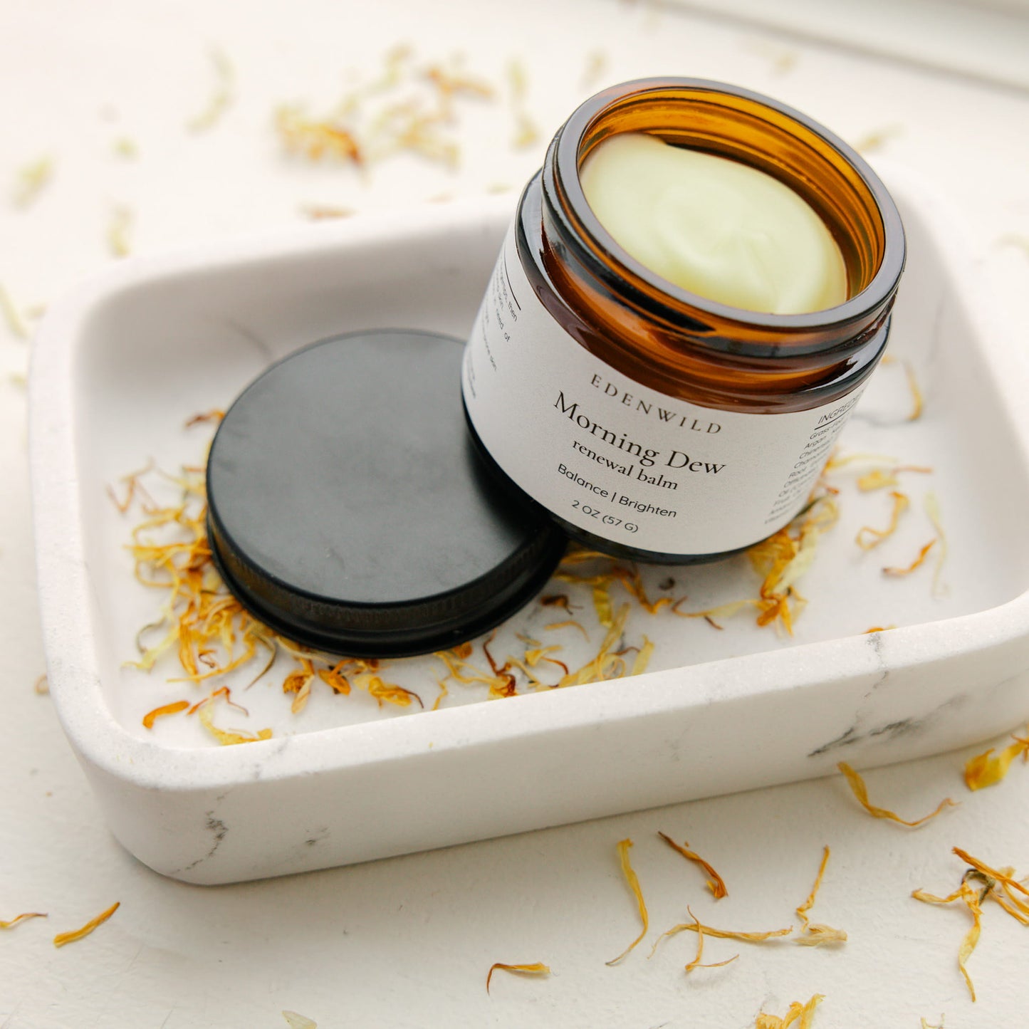Edenwild Morning Dew balm open on white ceramic dish with dried botanicals — tallow renewal balm for skin brightening and daily moisture