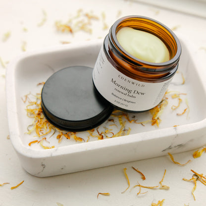 Edenwild Morning Dew balm open on white ceramic dish with dried botanicals — tallow renewal balm for skin brightening and daily moisture