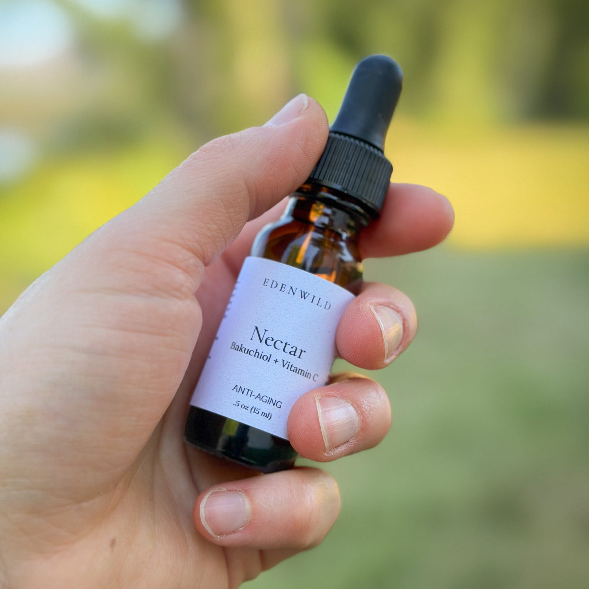 Hand holding Edenwild Nectar Bakuchiol + Vitamin C face serum 0.5 oz outdoors — natural retinol alternative serum for anti-aging and brightening mature skin