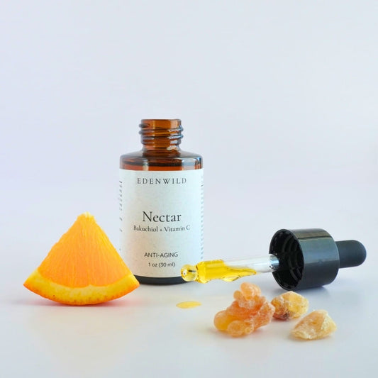 Close-up of glass pipette dripping golden serum beside fresh orange slice and frankincense resin on white background, showcasing the luxurious texture of Edenwild Nectar Face Serum to help brighten and rejuvenate mature skin