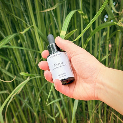 Hand holding Edenwild Nectar Bakuchiol + Vitamin C anti-aging face serum 1 oz in tall grass — natural retinol alternative serum for brightening and firming mature skin