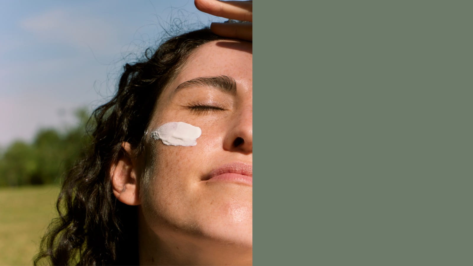 Woman applying Edenwild tallow balm outdoors in natural sunlight, eyes closed, with a swipe of white botanical cream on her cheek against a green Wyoming landscape background