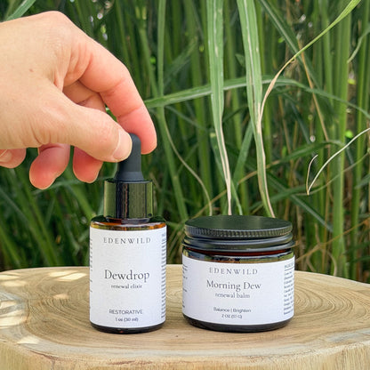 Hand holding Edenwild Dewdrop Face Serum dropper beside Morning Dew Tallow Balm on wood slice — natural two-step skincare routine for balanced, renewed skin