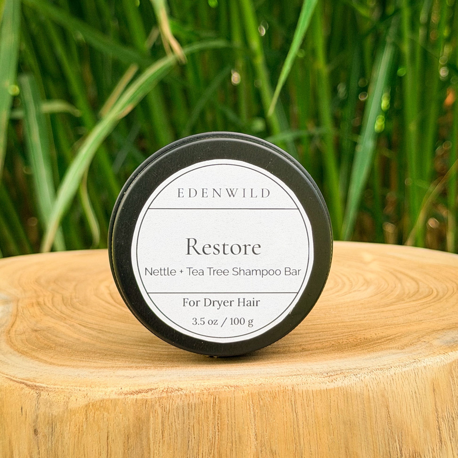 Edenwild Restore shampoo bar — nettle and tea tree natural shampoo bar for dry hair in reusable black tin on wood stump with wild grass background