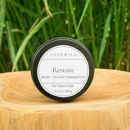 Edenwild Restore shampoo bar — nettle and tea tree natural shampoo bar for dry hair in reusable black tin on wood stump with wild grass background
